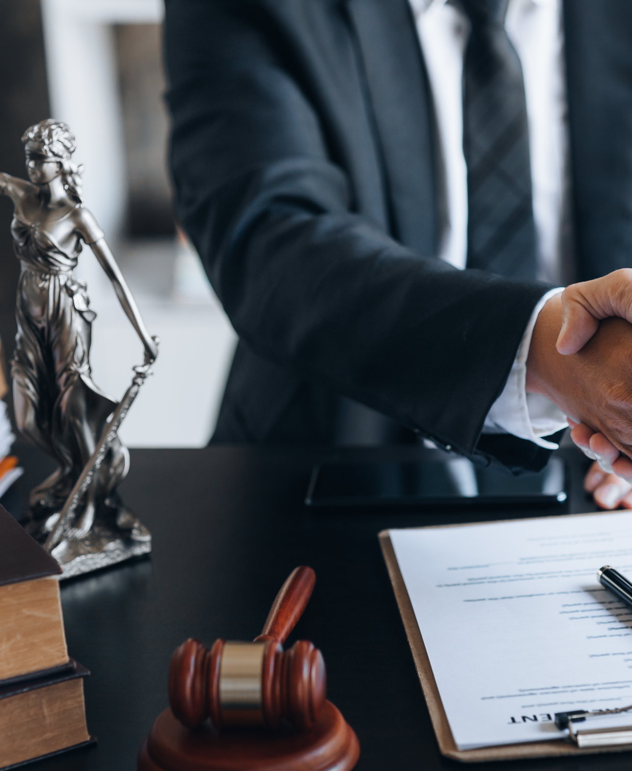 A client and their attorney shaking hands over a signed agreement, a statue of Lady Justice and a gavel on the desk &mdash; Essex County criminal defense