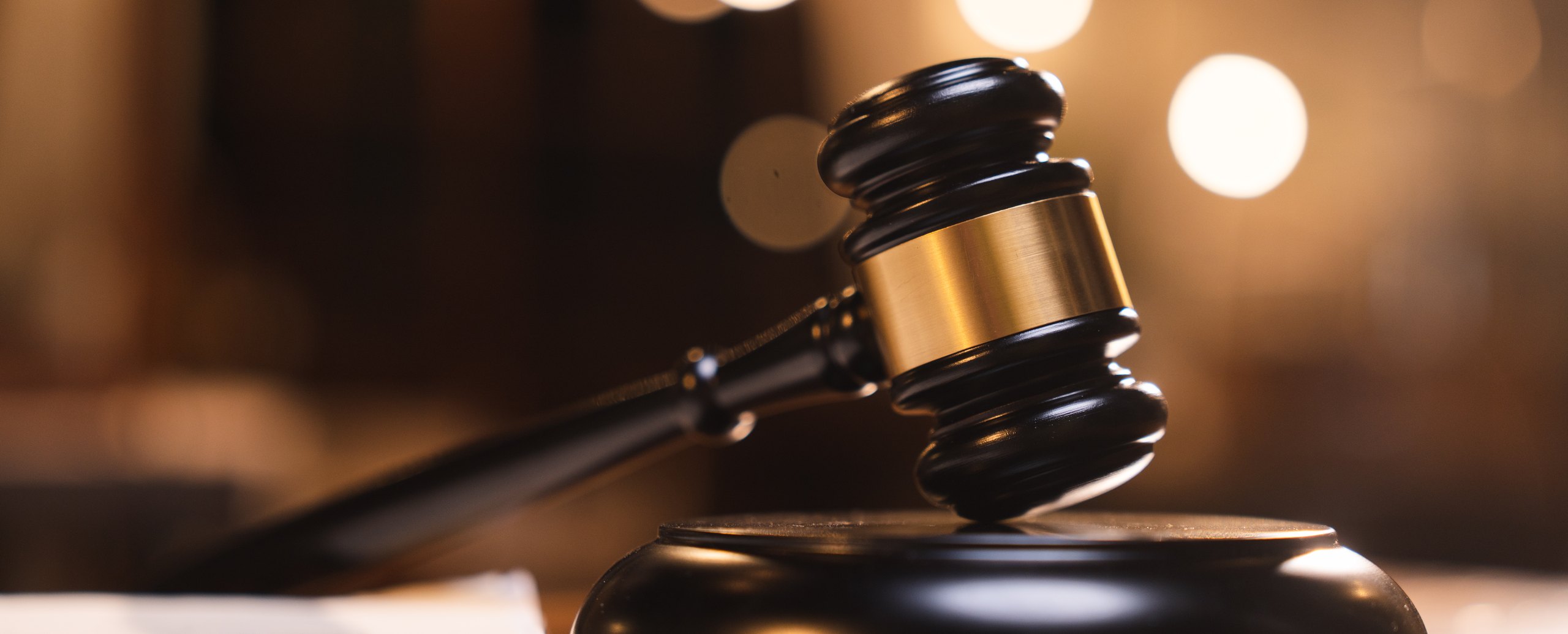 A judge&rsquo;s gavel resting on its block, warm courtroom lights blurred behind