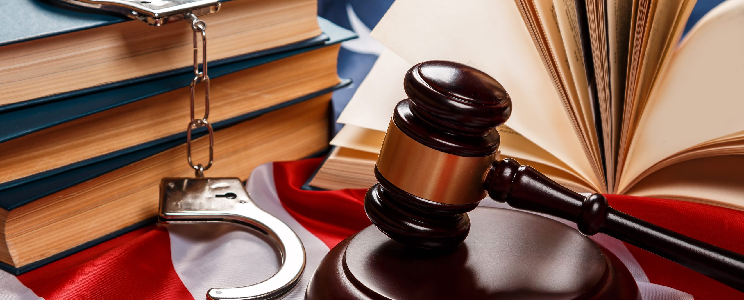 A gavel and handcuffs resting on an American flag beside a stack of law books
