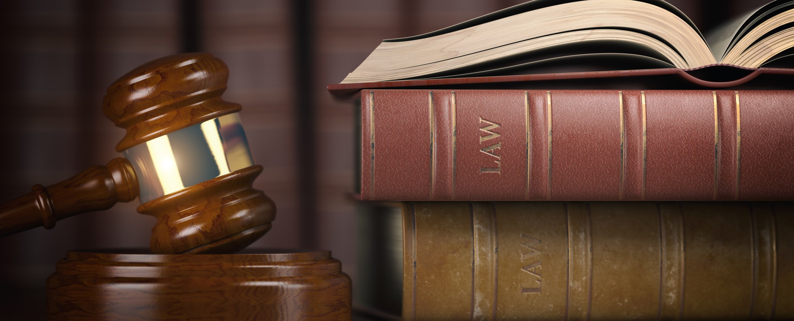 Law books stacked on a desk beside a gavel, an open book resting on top