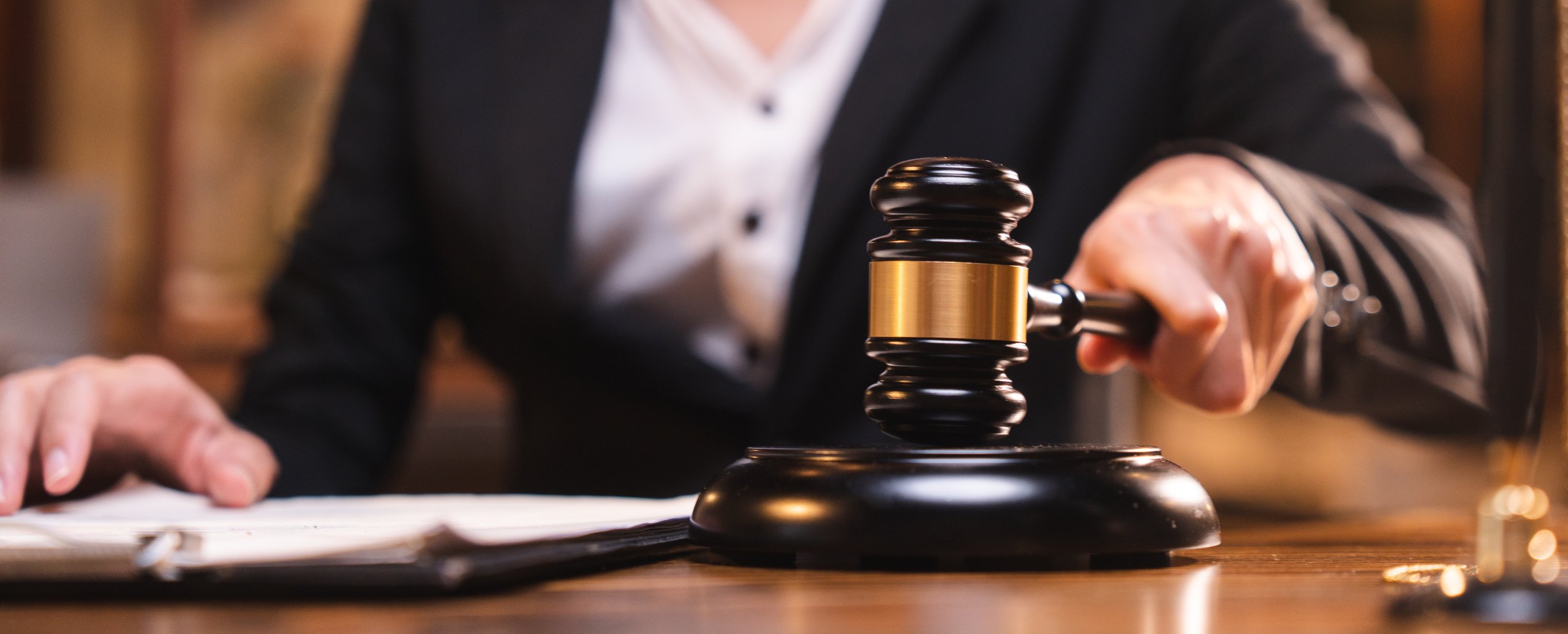 A judge striking a gavel at the bench, an open book and the scales of justice alongside