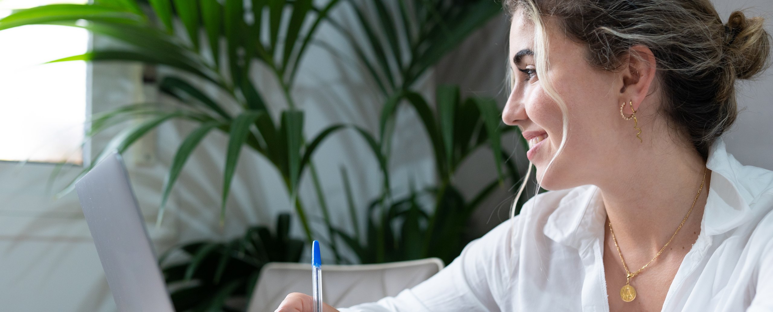 A woman smiling as she writes in a notebook beside a laptop