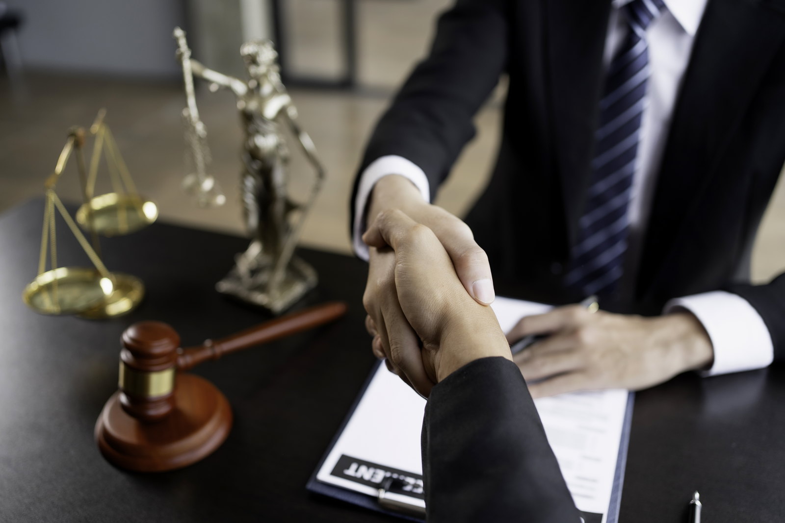 A handshake across a desk beside the scales of justice and a gavel — retaining counsel in North Bergen