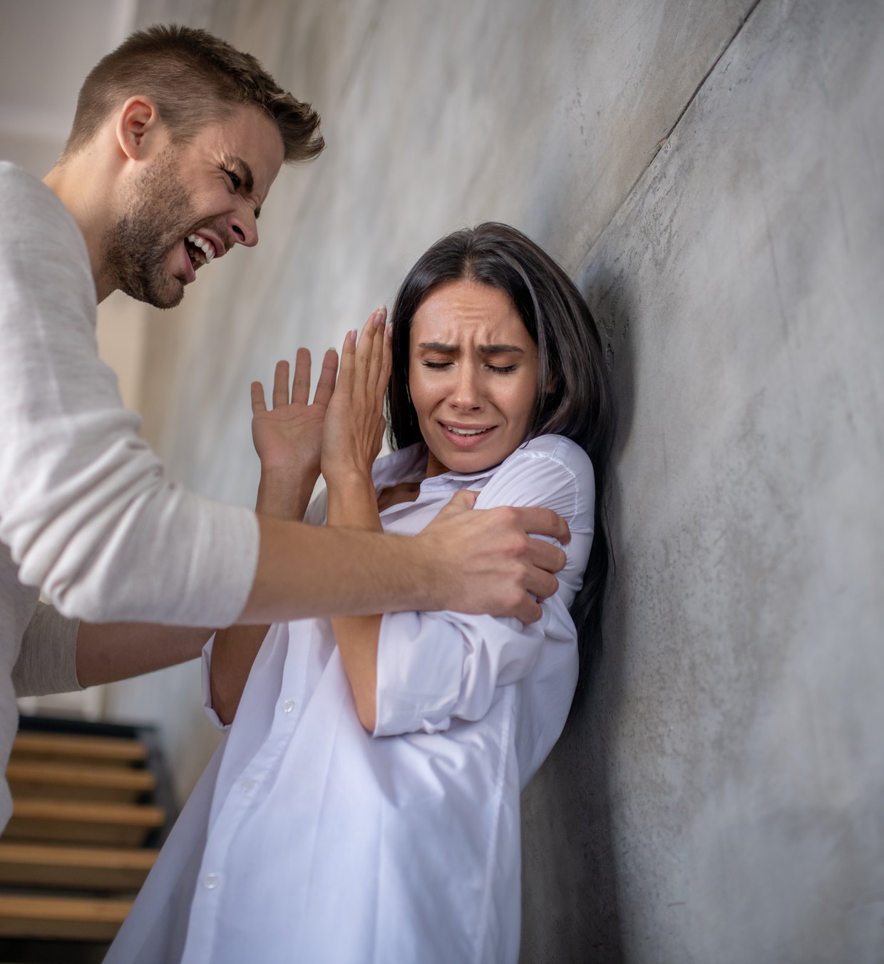 A man shouting at a woman who is shielding herself against a wall