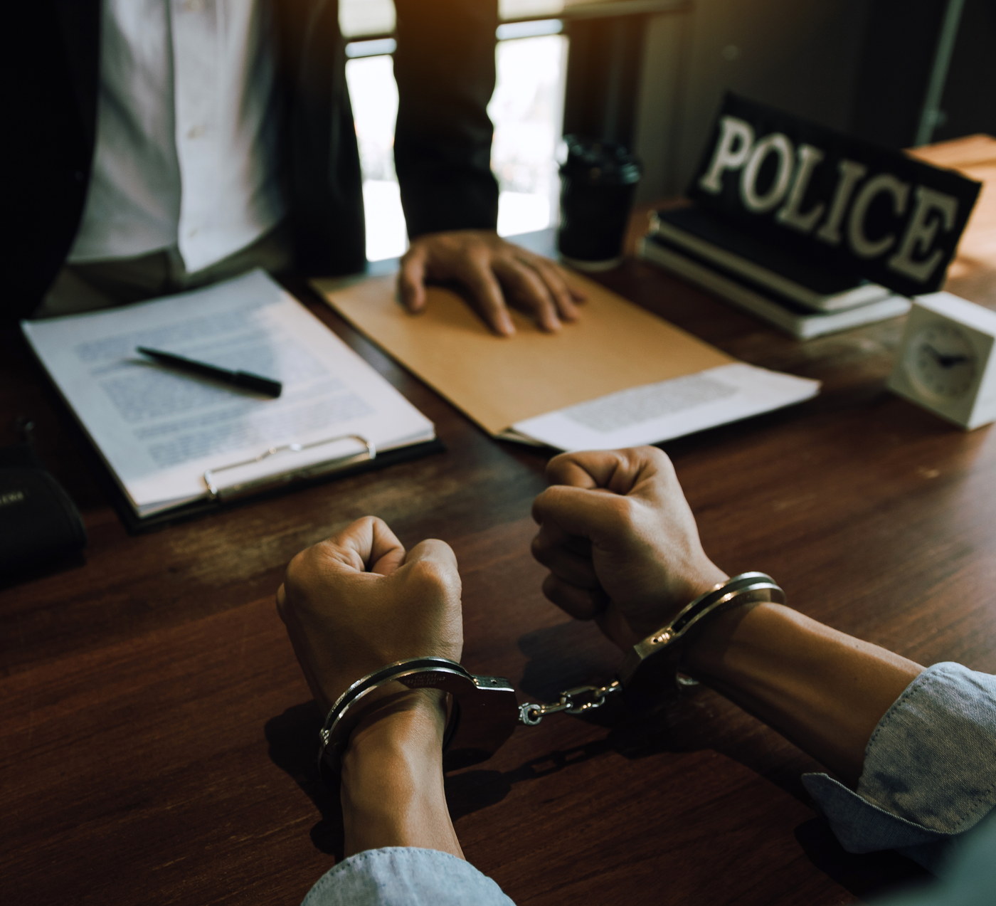 Handcuffed hands on a police interview table beside an officer&rsquo;s case file