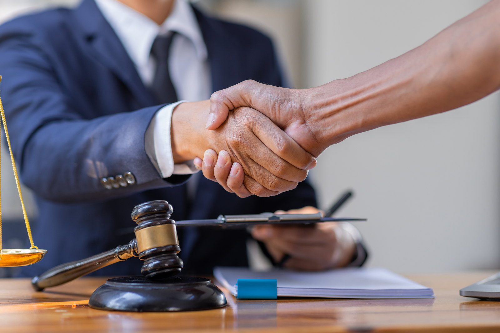 Handshake across a desk beside the scales of justice and a gavel