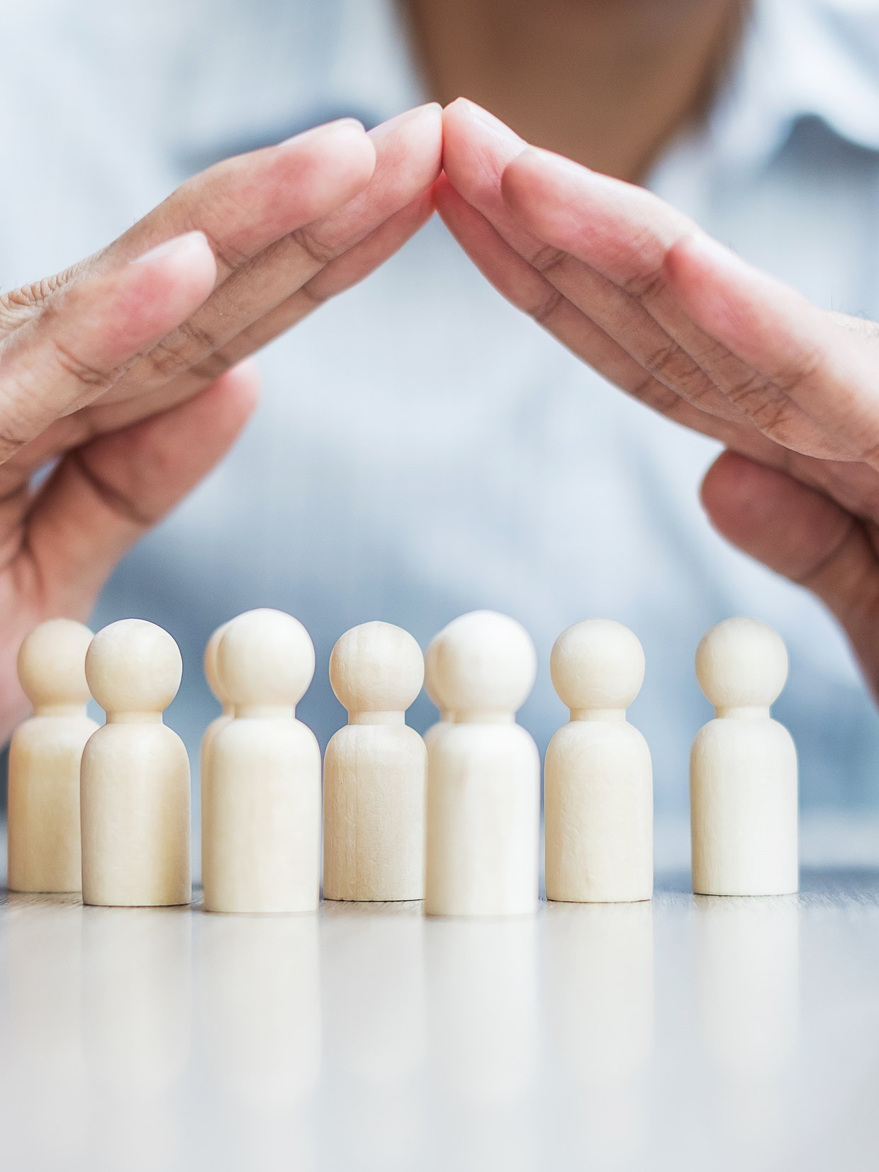 Hands held protectively over a row of wooden figures