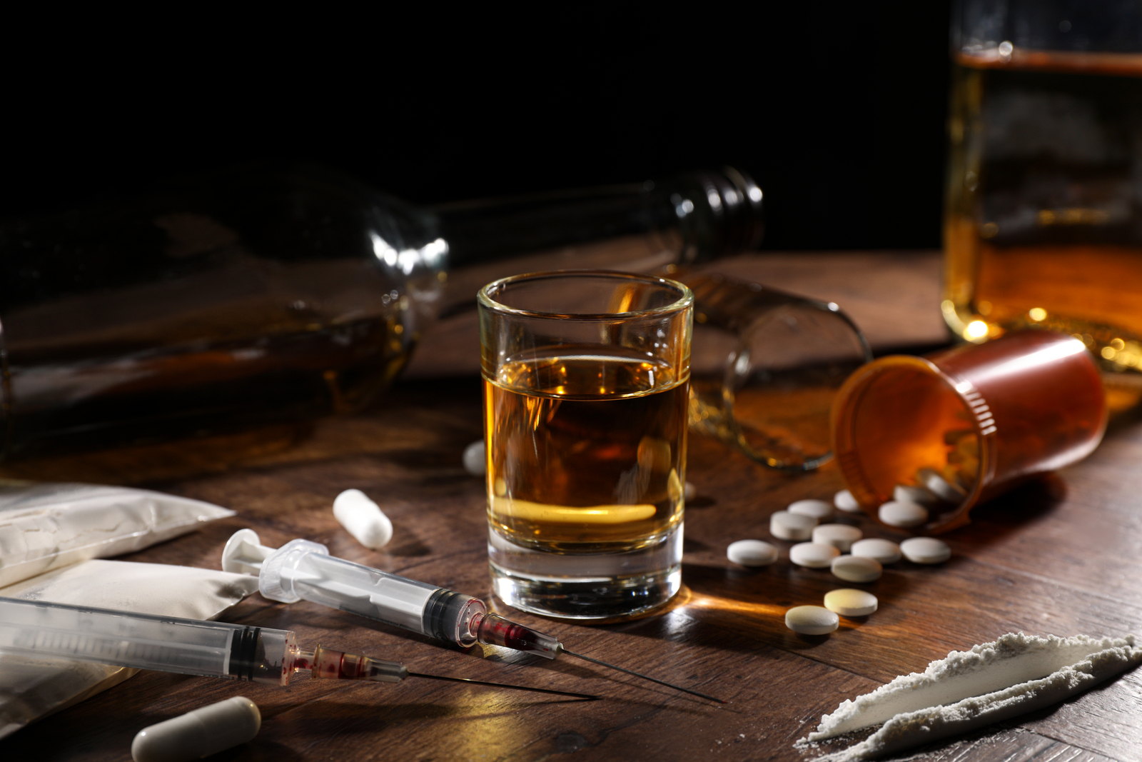 A glass, a pill bottle and loose tablets on a dark table