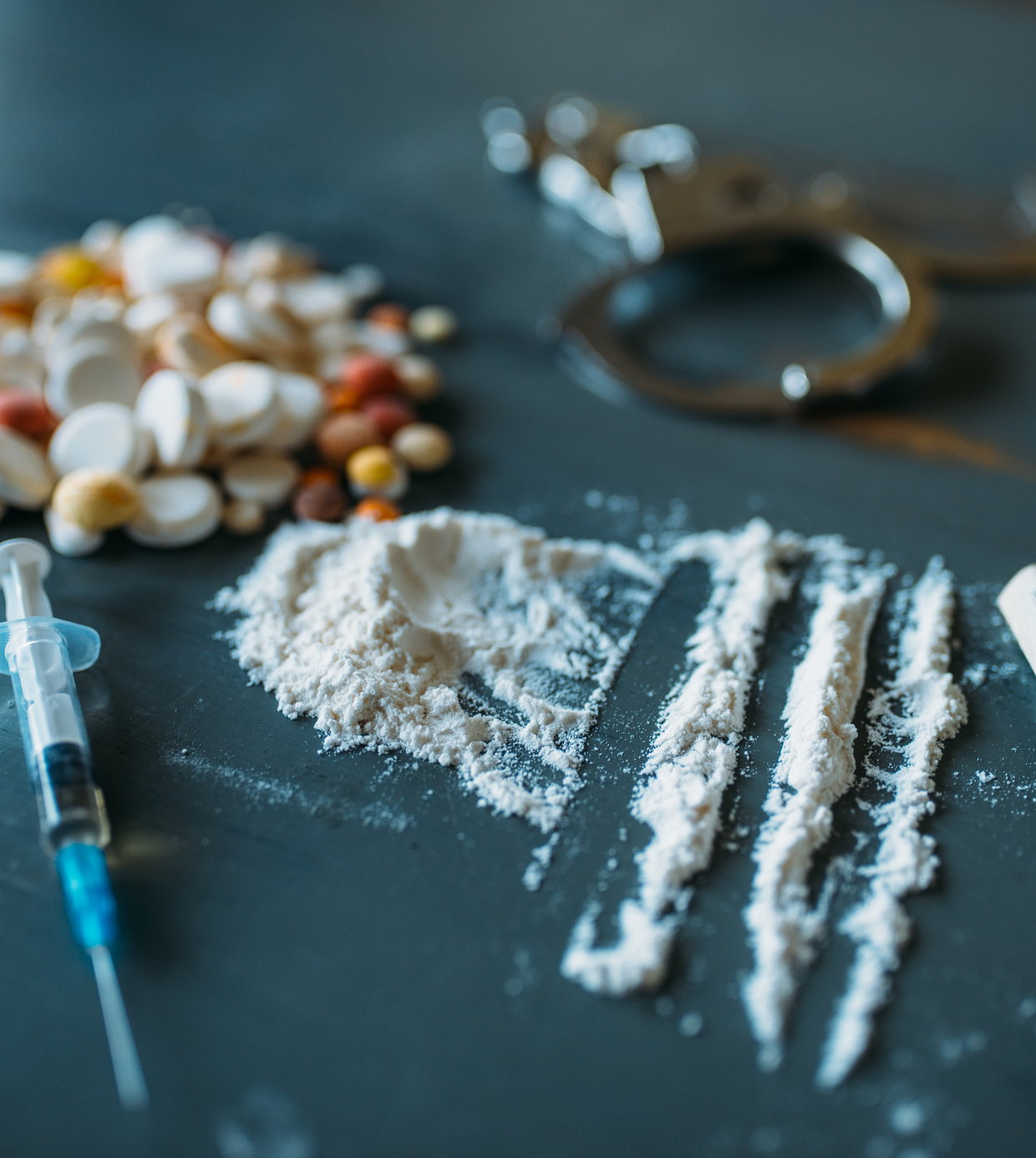 Pills, powder, a syringe and handcuffs on a dark table