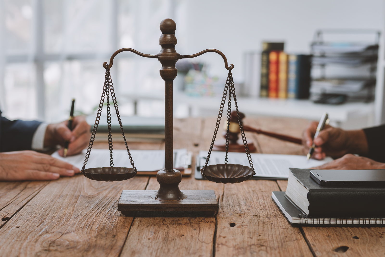 Two people signing papers at a table beside the scales of justice