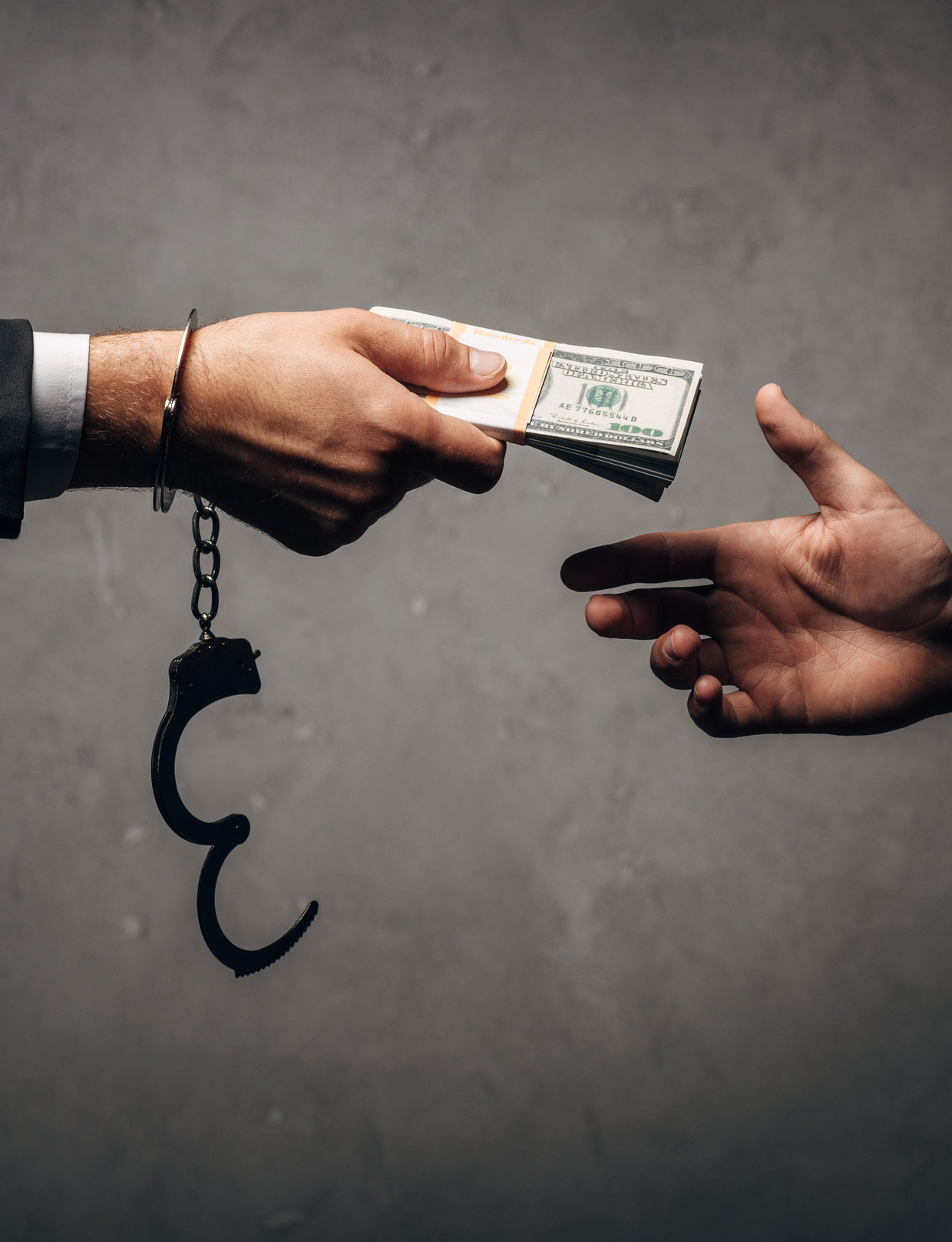 A bundle of banknotes passing between two hands, handcuffs alongside