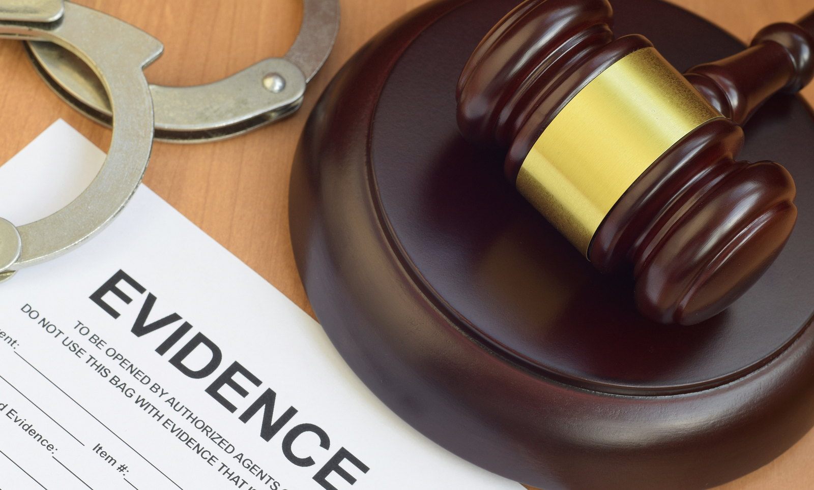 An evidence bag beside a gavel and handcuffs on a table