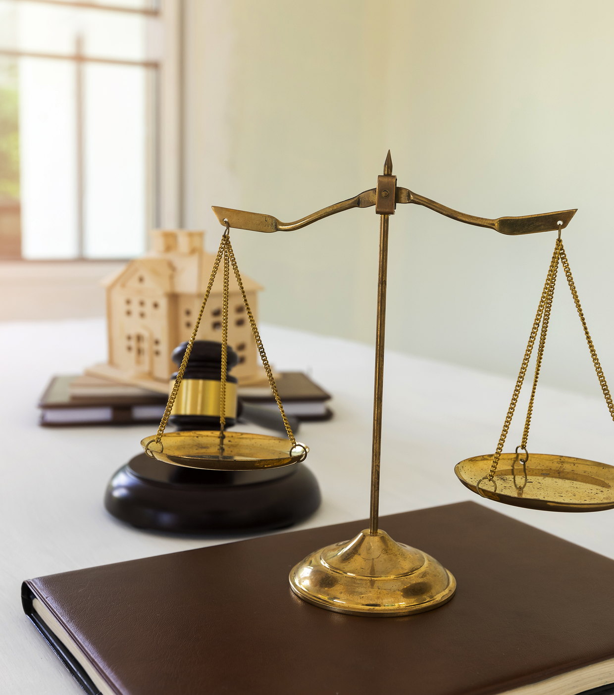 Scales of justice beside a small wooden house on a desk