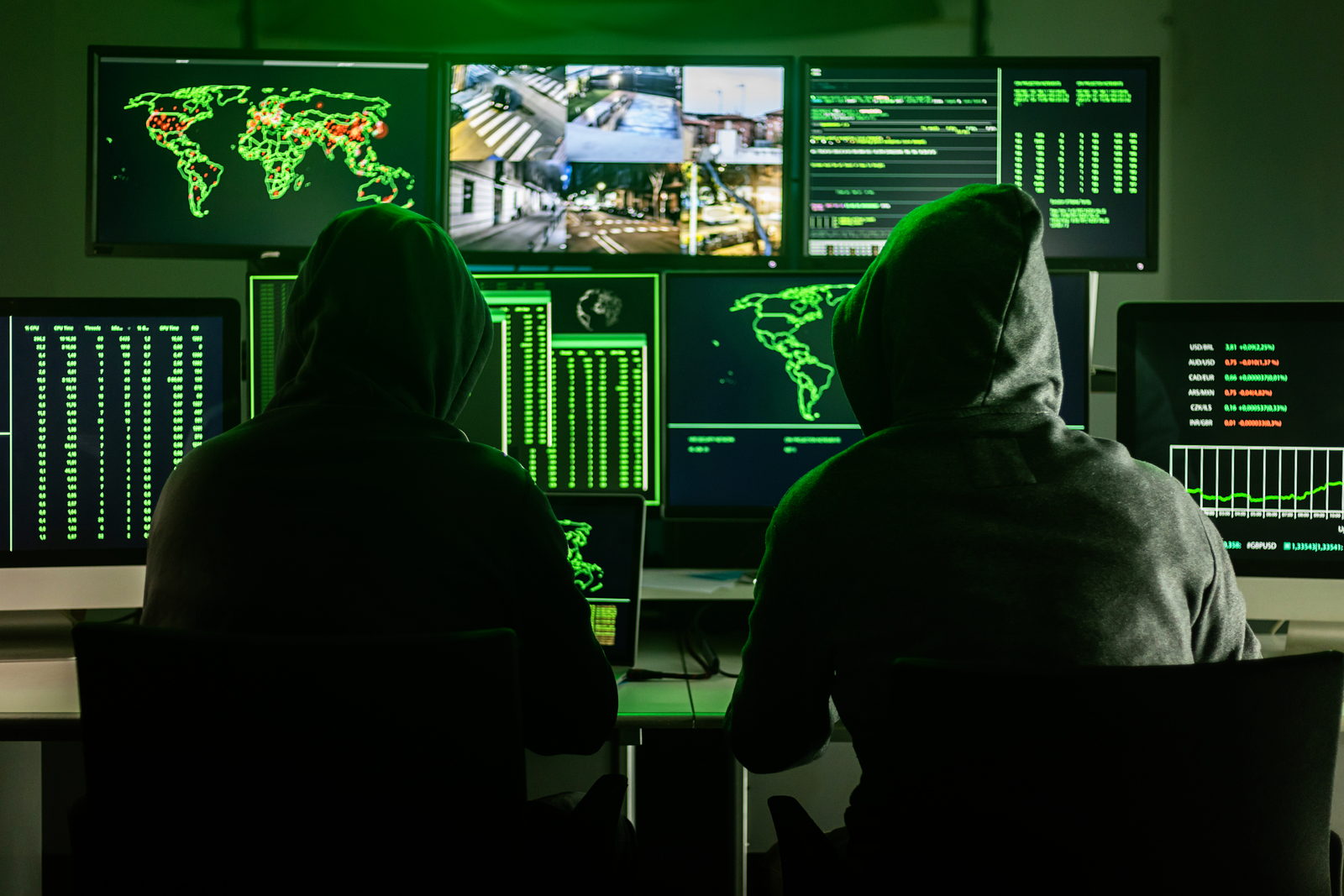 Two hooded figures at a bank of computer screens