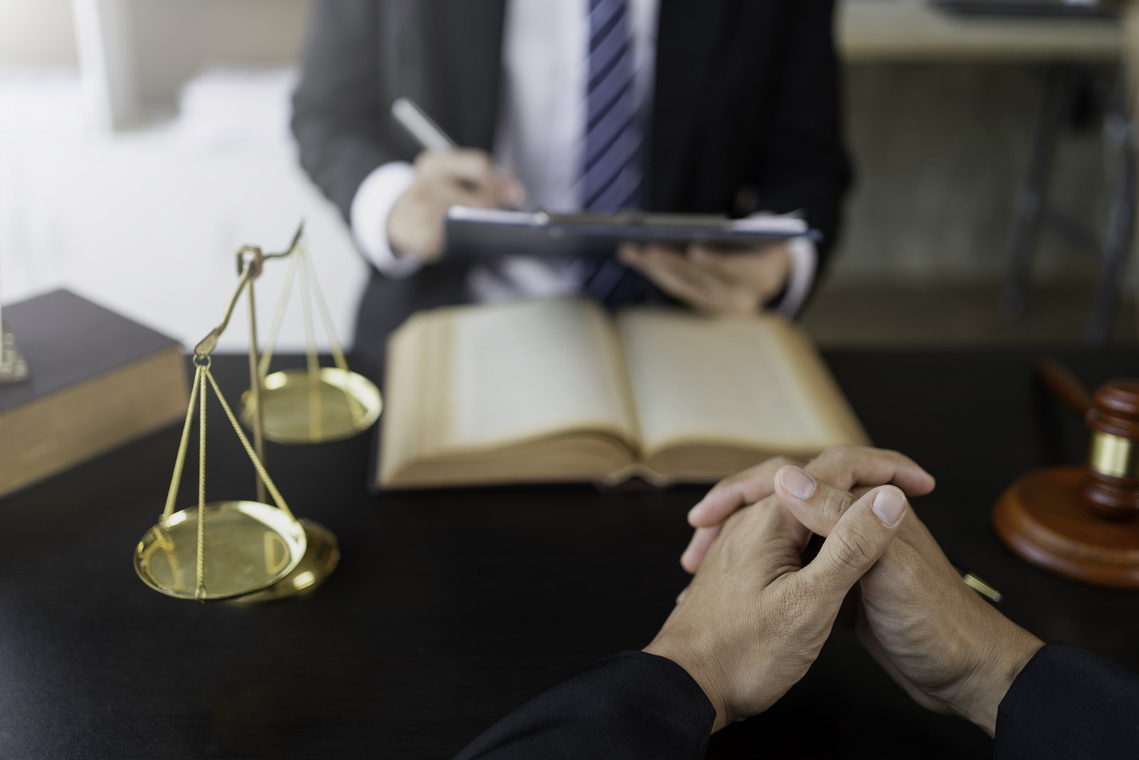 A client consulting a lawyer across a desk, scales and a law book alongside