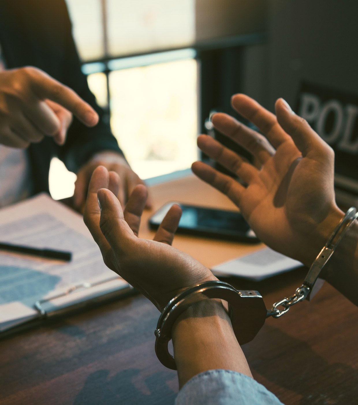 Hands raised across a desk at a police station, handcuffs on the wrist