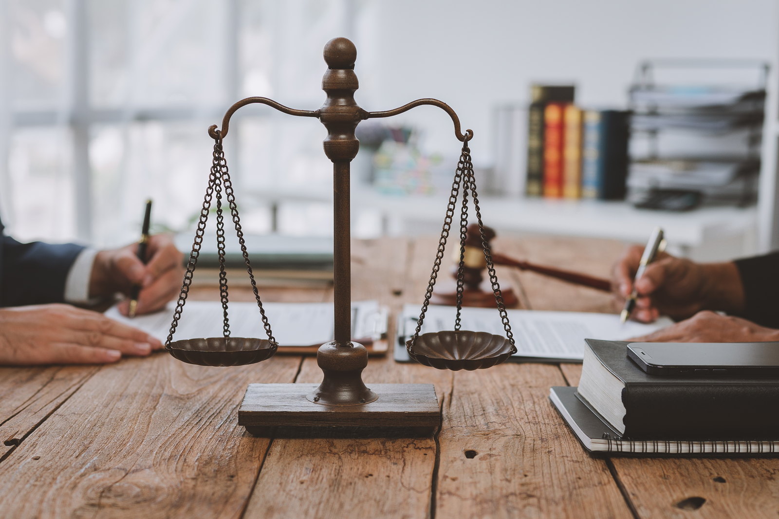 Scales of justice on a table as two people sign documents