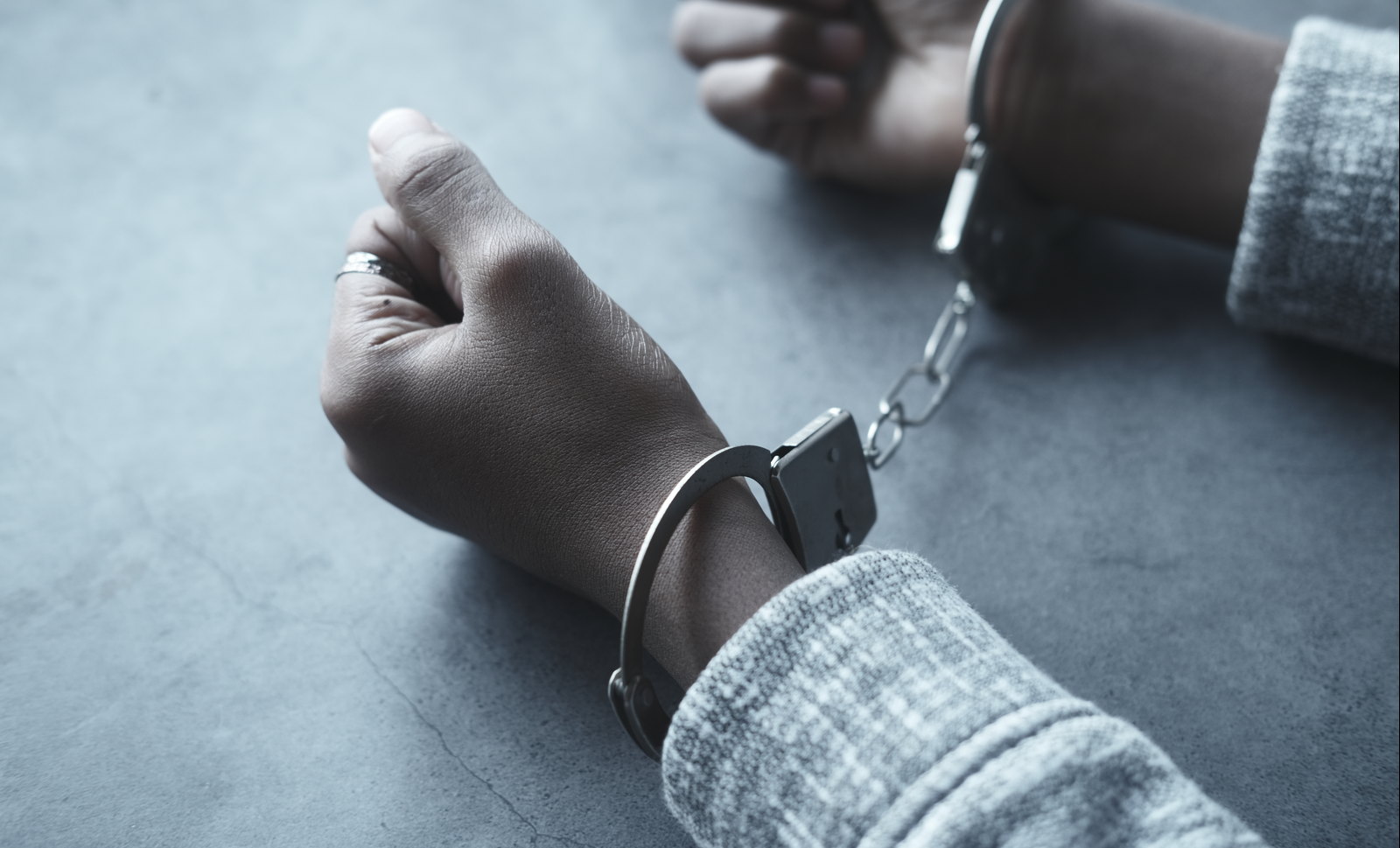 A handcuffed wrist resting on a grey surface